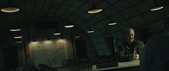 Movie still from “American Dharma” (2018), directed by Errol Morris – A group of chairs in a dark room with lights hanging from the ceiling; Wide shot, Over the shoulder angle