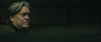 Movie still from “American Dharma” (2018), directed by Errol Morris – A person standing in front of a green wall; Close Up shot, Over the shoulder angle