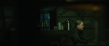 Movie still from “American Dharma” (2018), directed by Errol Morris – A man sitting at a table in front of a bar; Medium shot, Over the shoulder angle