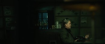 Movie still from “American Dharma” (2018), directed by Errol Morris – A man sitting at a table in front of a bar; Medium shot, Over the shoulder angle