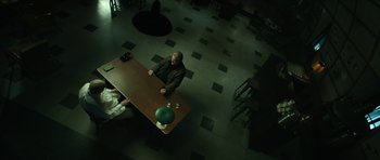 Movie still from “American Dharma” (2018), directed by Errol Morris – A man sitting at a table in a dark room; Wide shot, High angle