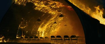 Movie still from “American Dharma” (2018), directed by Errol Morris – Chairs are lined up in front of a wall of fire; Extreme Wide shot, High angle