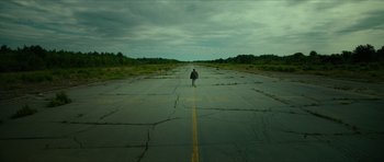 Movie still from “American Dharma” (2018), directed by Errol Morris – A person is walking down the middle of an empty road; Extreme Wide shot, High angle