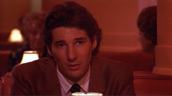 Movie still from “American Gigolo” (1980), directed by Paul Schrader – A man in a suit and tie sitting at a table; Close Up shot, Over the shoulder angle
