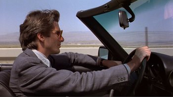 Movie still from “American Gigolo” (1980), directed by Paul Schrader – A man in a suit driving a car on a road; Medium shot, Low angle