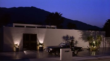 Movie still from “American Gigolo” (1980), directed by Paul Schrader – A man standing next to a car in front of a building; Extreme Wide shot, Low angle