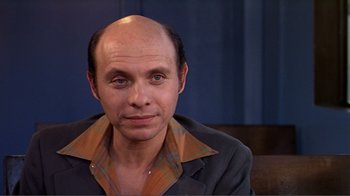 Movie still from “American Gigolo” (1980), directed by Paul Schrader – A man with a bald head sitting in front of a curtain; Close Up shot, High angle