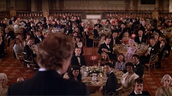 Movie still from “American Gigolo” (1980), directed by Paul Schrader – A crowd of people sitting at tables in a room; Wide shot, Over the shoulder angle
