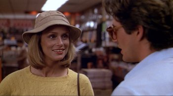 Movie still from “American Gigolo” (1980), directed by Paul Schrader – A woman wearing a tan hat and a yellow sweater talking to a man wearing glasses; Close Up shot, Over the shoulder angle