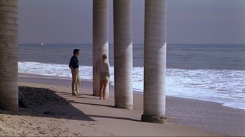 Movie still from “American Gigolo” (1980), directed by Paul Schrader – Two people standing on a beach near pillars; Wide shot, High angle