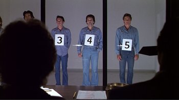 Movie still from “American Gigolo” (1980), directed by Paul Schrader – A group of men standing next to each other with numbers on them; Medium shot, Over the shoulder angle