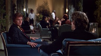 Movie still from “American Gigolo” (1980), directed by Paul Schrader – A group of people sitting around a room; Medium shot, Over the shoulder angle