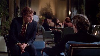 Movie still from “American Gigolo” (1980), directed by Paul Schrader – A man in a suit and tie sitting next to another man in a suit and tie; Medium shot, Over the shoulder angle