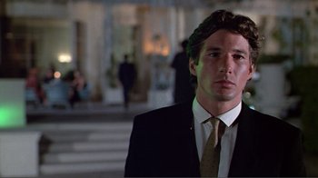 Movie still from “American Gigolo” (1980), directed by Paul Schrader – A man in a suit and tie standing in front of a building; Close Up shot, Low angle