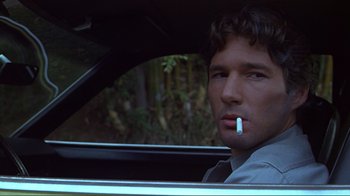 Movie still from “American Gigolo” (1980), directed by Paul Schrader – A man sitting in the drivers seat of a car smoking a cigarette; Close Up shot, Low angle