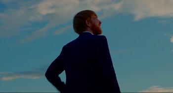 Movie still from “American Made” (2017), directed by Doug Liman – A man with a red beard standing in front of a blue sky; Medium shot, Low angle
