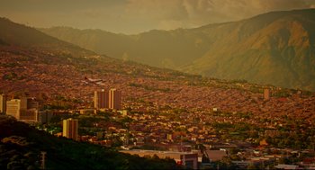 Movie still from “American Made” (2017), directed by Doug Liman – An airplane flying over a city with a mountain in the background; Extreme Wide shot, High angle