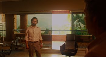 Movie still from “American Made” (2017), directed by Doug Liman – A man standing in front of a chair in front of a window; Wide shot, Low angle