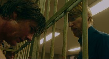 Movie still from “American Made” (2017), directed by Doug Liman – Two men standing next to each other behind a metal fence; Medium shot, Over the shoulder angle