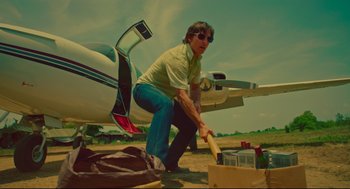 Movie still from “American Made” (2017), directed by Doug Liman – A man in a green shirt is holding a baseball bat in front of an airplane; Medium shot, Low angle