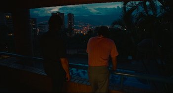 Movie still from “American Made” (2017), directed by Doug Liman – Two men looking out over a city at night; Wide shot, Over the shoulder angle