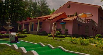 Movie still from “American Made” (2017), directed by Doug Liman – A woman walking on a path in front of a pink house; Extreme Wide shot, High angle