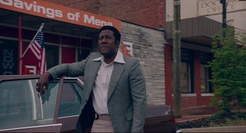 Movie still from “American Made” (2017), directed by Doug Liman – A man standing next to a car in front of a building; Medium shot, Low angle