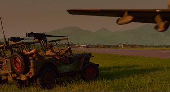 Movie still from “American Made” (2017), directed by Doug Liman – An old jeep is parked in the grass near an airplane; Extreme Wide shot, Low angle
