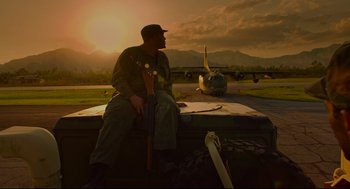 Movie still from “American Made” (2017), directed by Doug Liman – A man sitting on top of a truck near an airplane; Wide shot, Low angle