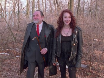 An older man and a younger woman standing next to each other in the woods