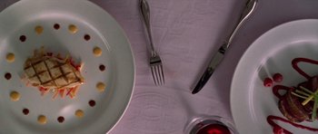 Movie still from “American Psycho” (2000), directed by Mary Harron – A table with a plate , fork , knife and a glass of red wine; Extreme Close Up shot, Overhead angle
