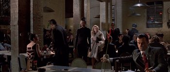 Movie still from “American Psycho” (2000), directed by Mary Harron – A group of people standing around a room; Wide shot, Over the shoulder angle