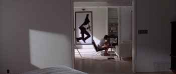 Movie still from “American Psycho” (2000), directed by Mary Harron – A man sitting in a chair in front of a painting; Wide shot, High angle