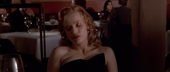 Movie still from “American Psycho” (2000), directed by Mary Harron – A woman in a black dress sitting in front of a table; Close Up shot, Low angle