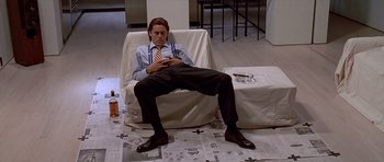 Movie still from “American Psycho” (2000), directed by Mary Harron – A man sitting on a couch looking at his cell phone; Medium shot, High angle