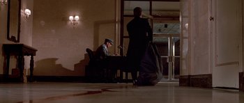 Movie still from “American Psycho” (2000), directed by Mary Harron – A man sitting at a table in front of a door; Wide shot, Low angle