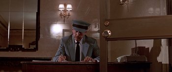 Movie still from “American Psycho” (2000), directed by Mary Harron – A man in a hat and suit writing on a piece of paper in front of a mirror; Medium shot, Low angle