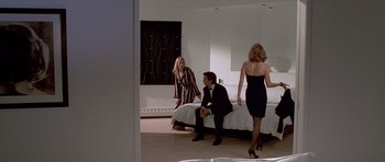Movie still from “American Psycho” (2000), directed by Mary Harron – A man sitting on a bed next to two women in a room; Wide shot, Over the shoulder angle