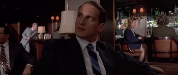 Movie still from “American Psycho” (2000), directed by Mary Harron – A man in a suit and tie sitting in front of a lamp; Close Up shot, Over the shoulder angle