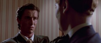 Movie still from “American Psycho” (2000), directed by Mary Harron – A man in a suit and tie looking at another man in a suit and tie in front of a mirror; Close Up shot, Over the shoulder angle