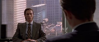Movie still from “American Psycho” (2000), directed by Mary Harron – A man in a suit and tie sitting in front of a window; Medium shot, Over the shoulder angle