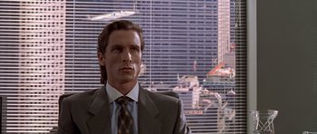 Movie still from “American Psycho” (2000), directed by Mary Harron – A man in a suit and tie in front of a window; Medium shot, Low angle
