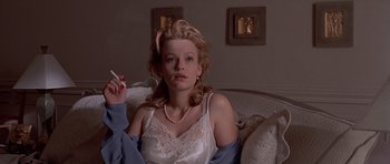 Movie still from “American Psycho” (2000), directed by Mary Harron – A woman sitting on top of a couch holding a cigarette; Medium shot, Low angle