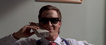Movie still from “American Psycho” (2000), directed by Mary Harron – A man wearing a tie and sunglasses holding a phone up to his ear; Medium shot, Low angle
