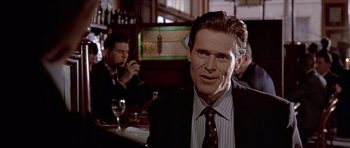 Movie still from “American Psycho” (2000), directed by Mary Harron – A man sitting at a table in front of a bar; Close Up shot, Over the shoulder angle
