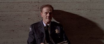 Movie still from “American Psycho” (2000), directed by Mary Harron – A man in a police uniform is holding a newspaper; Close Up shot, Low angle