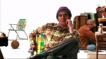 Movie still from “American Splendor” (2003), directed by Shari Springer Berman – A man sitting on a chair wearing a plaid shirt; Medium shot, Low angle