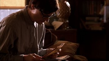 Movie still from “American Splendor” (2003), directed by Shari Springer Berman – A man sitting on a bed looking at a book; Medium shot, High angle