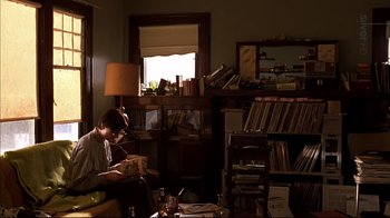Movie still from “American Splendor” (2003), directed by Shari Springer Berman – A man sitting in a living room reading a book; Wide shot, High angle