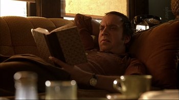 Movie still from “American Splendor” (2003), directed by Shari Springer Berman – A man reading a book while sitting on a couch; Medium shot, Low angle